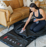 The sauna blanket laid out on a floor, showing how it fits into a home environment and can be used for at-home spa experiences